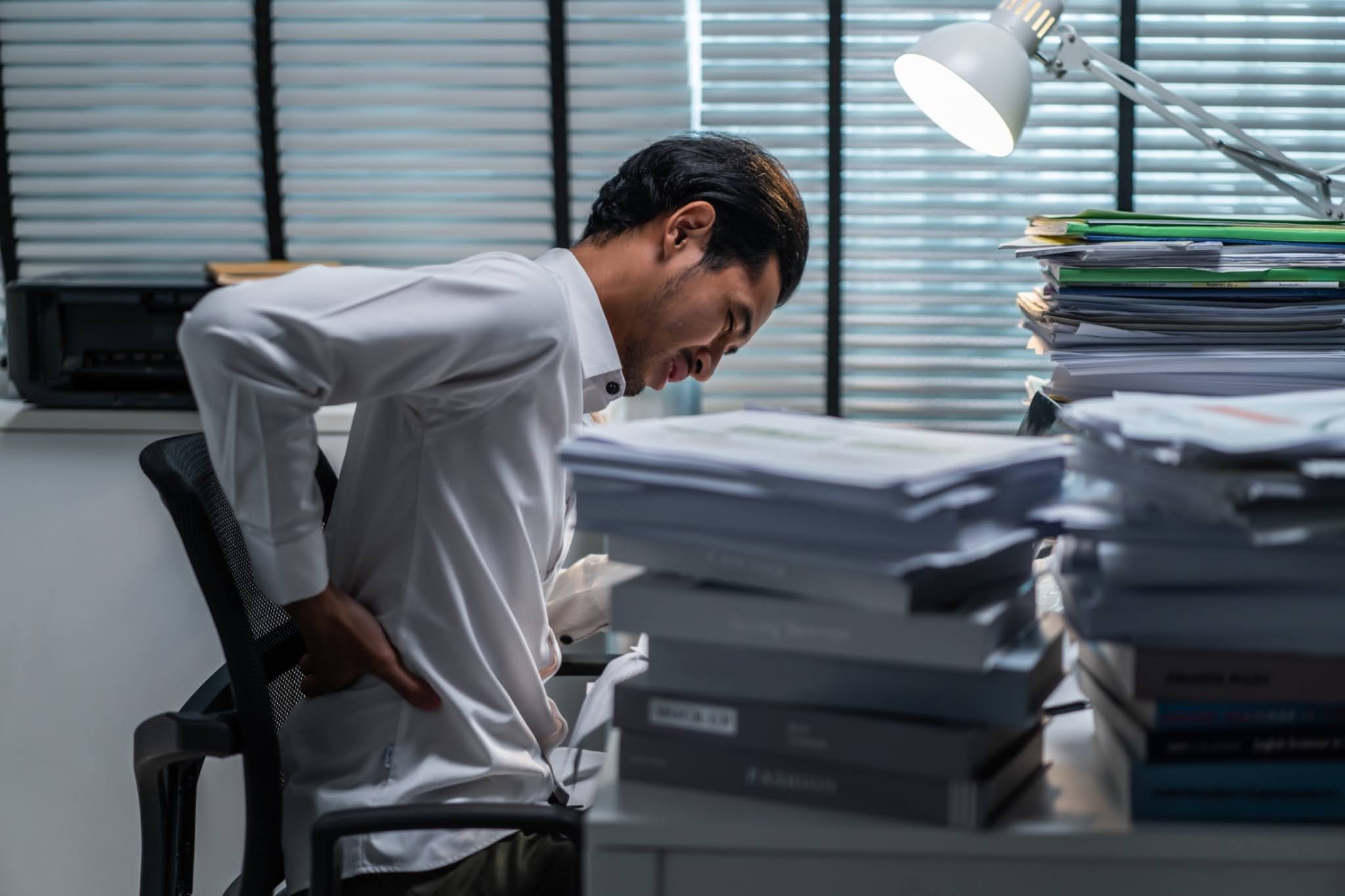Office worker experiencing lower back pain at desk with paperwork